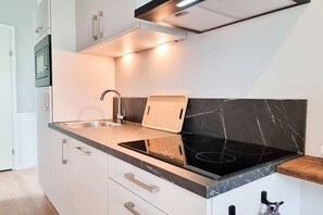 Una cocina moderna con estufa integrada, tabla de cortar de madera y pileta de acero inoxidable.