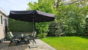 An outdoor patio with a table and chairs, a large umbrella, and a well-maintained lawn. - OK40 Chalet Oostkapelle (Oostkapelle)