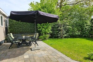 An outdoor patio with a table and chairs, a large umbrella, and a well-maintained lawn. - OK40 Chalet Oostkapelle (Oostkapelle)