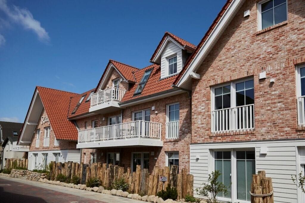 A row of brick townhouses with balconies, a stone wall, and a clear blue sky.