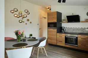 A modern kitchen with a dining area, wooden cabinets, a flat-screen TV, and a unique spherical light fixture. - Nautimar Apartment Kattegat 32 (Büsum)