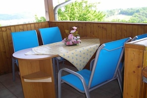 A wooden table with a floral tablecloth, blue chairs, and a view of greenery through a window. - Holiday apartment with 3 bedrooms (St. Stefan i \/R)
