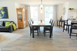 Un coin repas avec une longue table et des chaises, un buffet avec des portes en verre et un canapé avec des coussins.