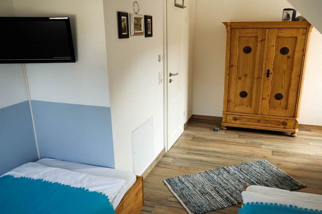 A bedroom with a bed, a wardrobe, a television mounted on the wall, and a wooden cabinet.