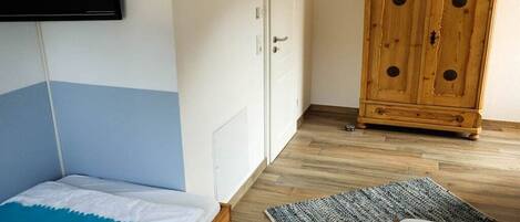 Quarto com cama, guarda-roupa, televisão na parede e um armário de madeira.