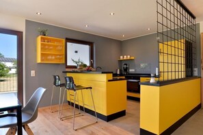 Una cocina moderna con una isla amarilla, taburetes de bar y vistas a través de un ventanal.