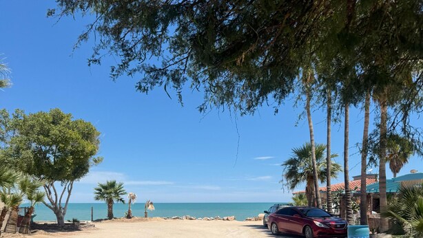 Ein Parkplatz am Strand mit einem roten Auto, Palmen und freiem Blick auf das Meer.