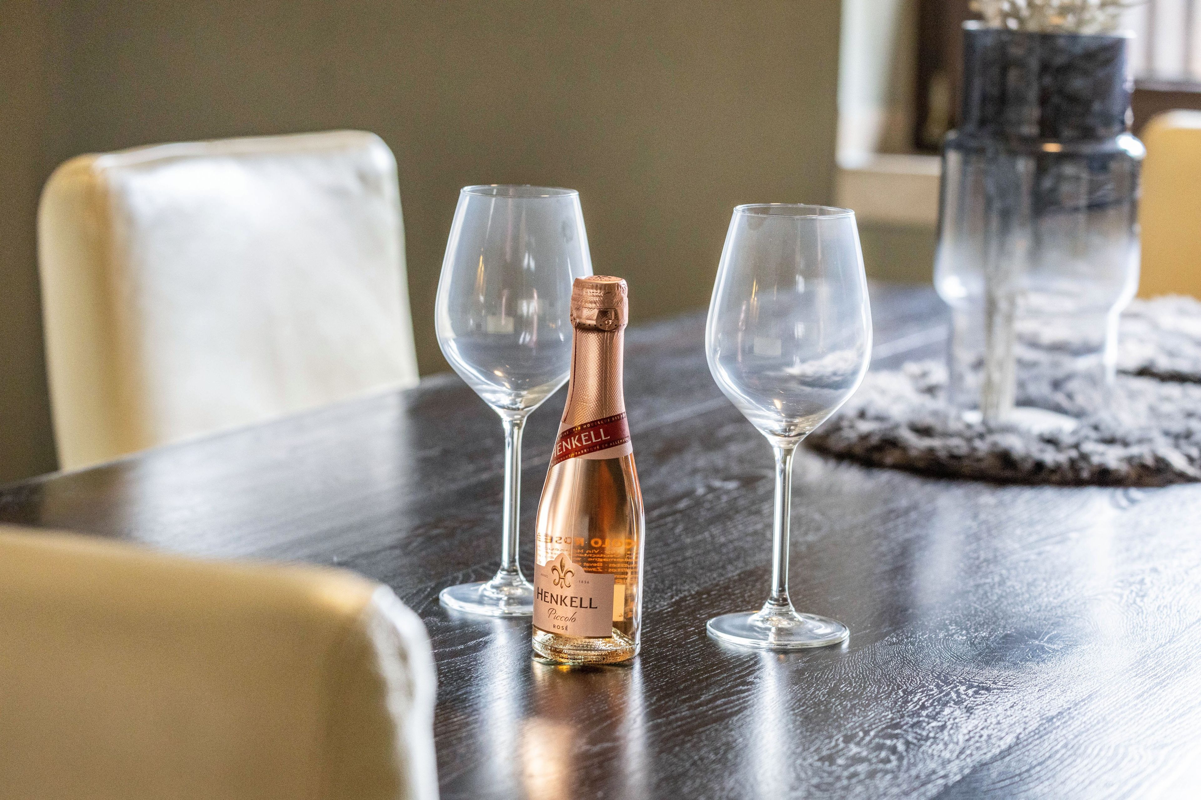 A bottle of Henkell Piccolo Rosé champagne on a table with two empty wine glasses.