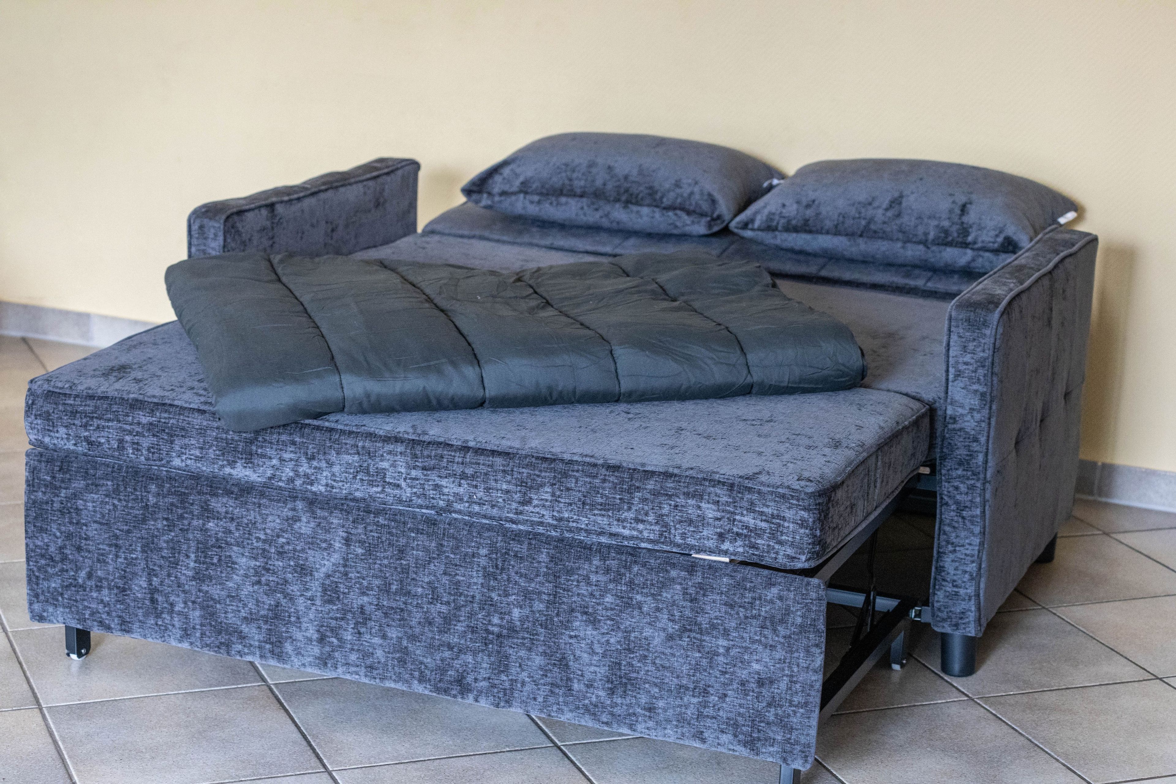 Una cama con cabecera y piecera tapizados en gris, un colchón gris y dos almohadas grises.