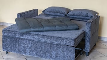 A bed with a grey upholstered headboard and footboard, a grey mattress, and two grey pillows.