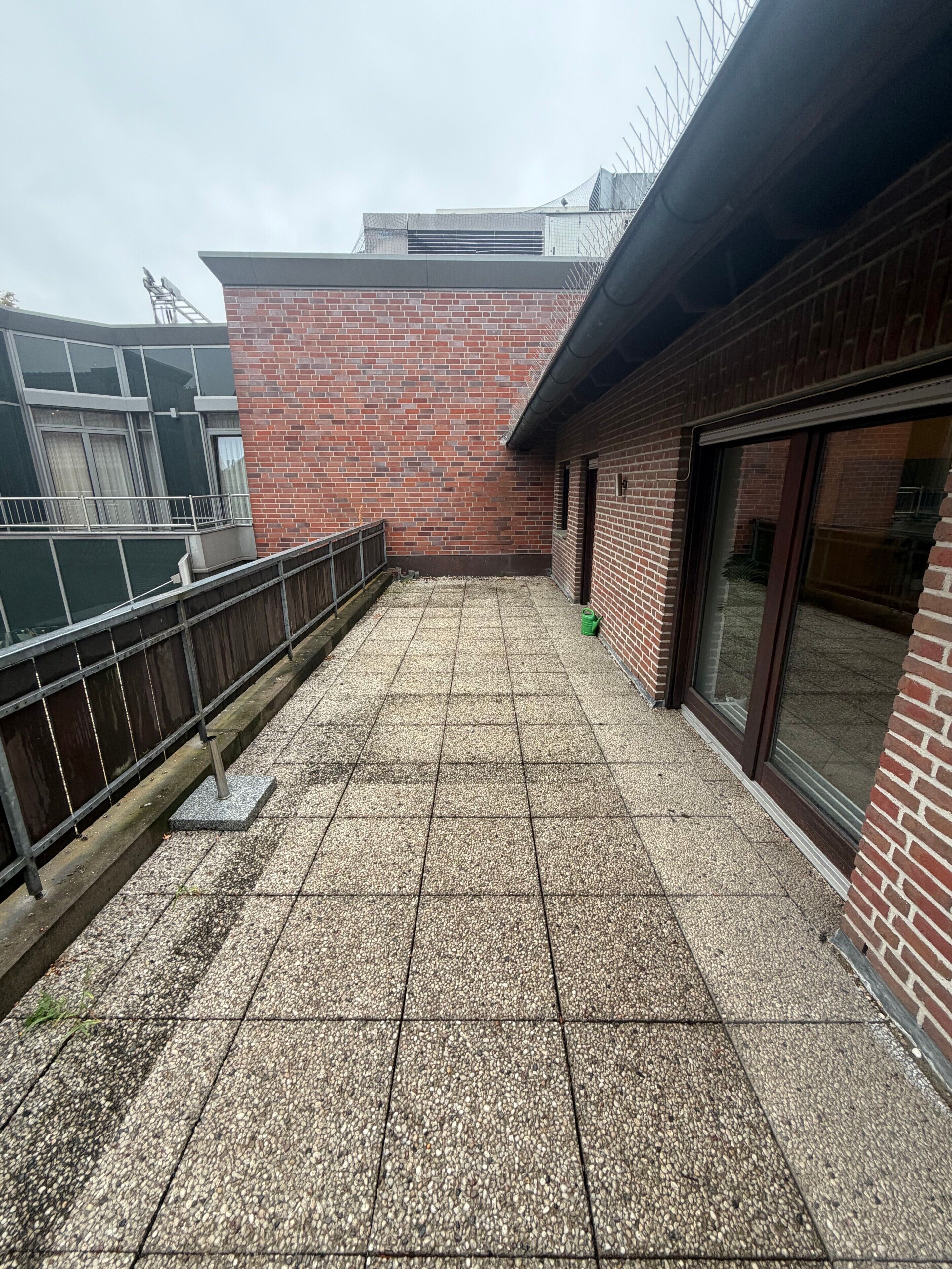 A rooftop terrace with a tiled floor, a brick wall, and a metal railing.