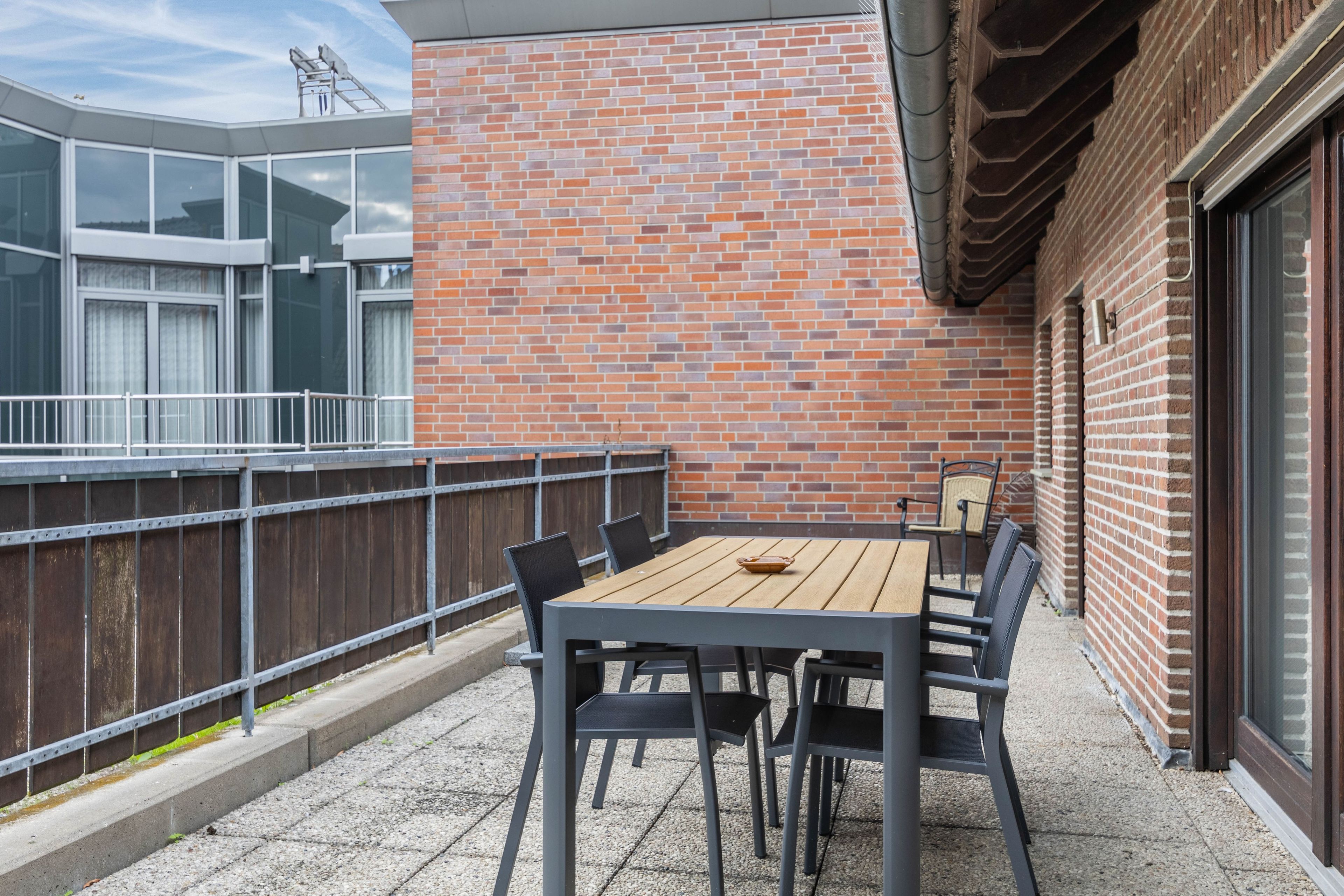 A rooftop terrace with a brick wall, a wooden table with chairs, and a metal railing.