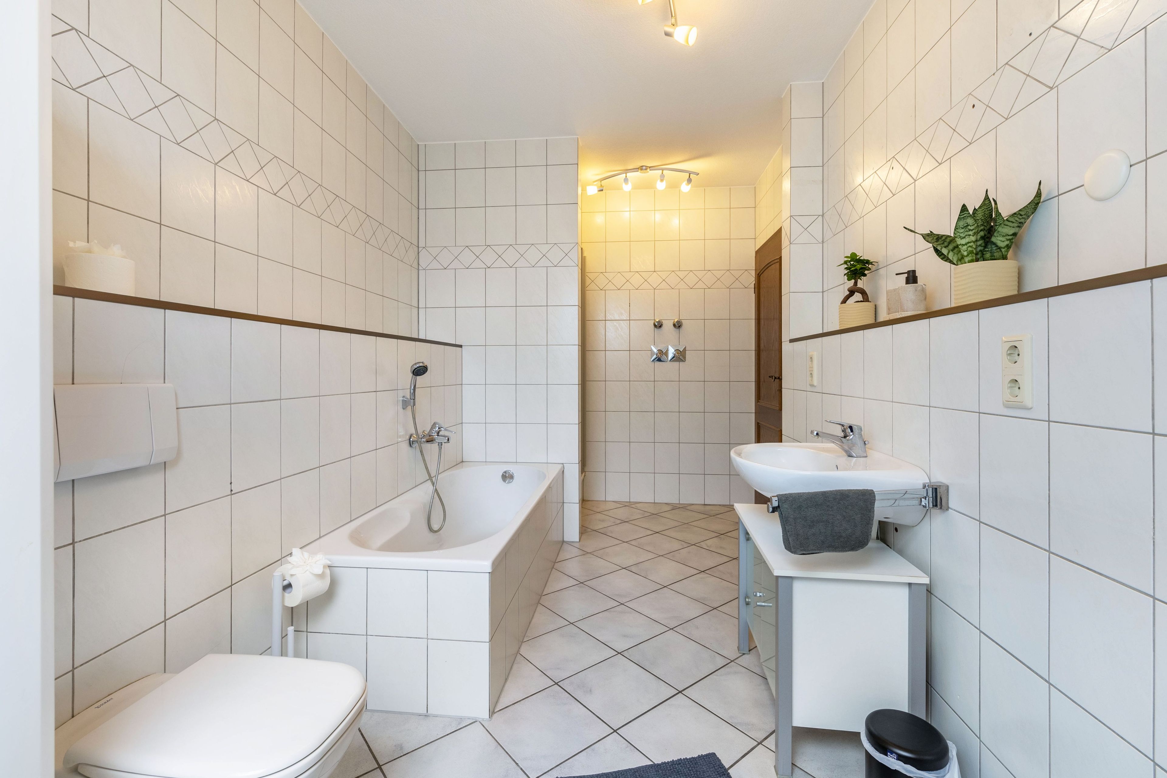 Ein modernes Badezimmer mit Badewanne, Toilette und Waschbecken, mit weißen Fliesen und einem geometrischen Muster an den Wänden.