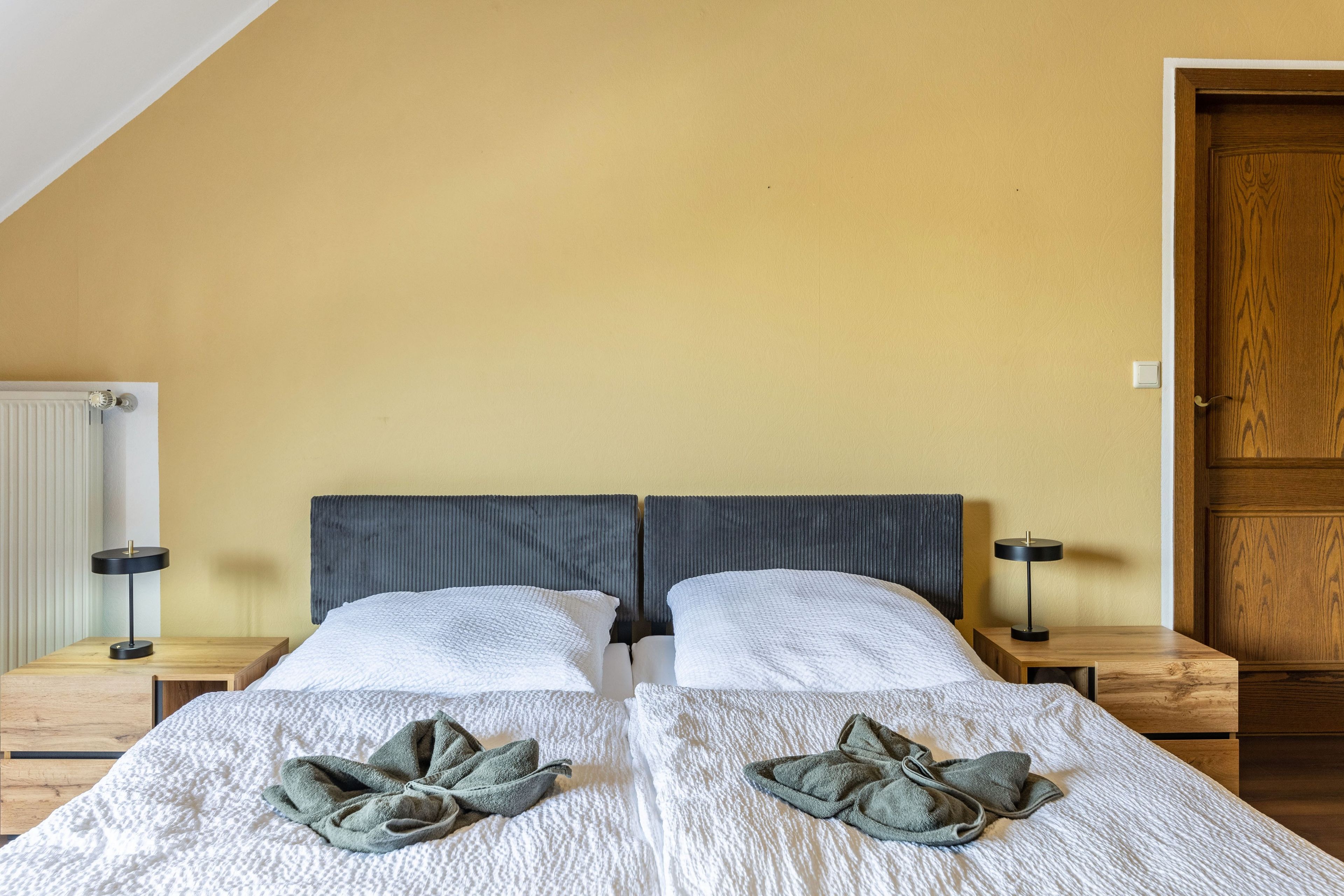 Ein Doppelbett mit weißer, strukturierter Bettdecke, zwei Kissen und zwei auf dem Bett gefalteten Handtüchern.