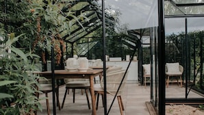 A conservatory with a glass ceiling, wooden furniture, and plants.