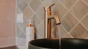 Een badkamer met een moderne kraan, een zeepdispenser en een zwarte wastafel.