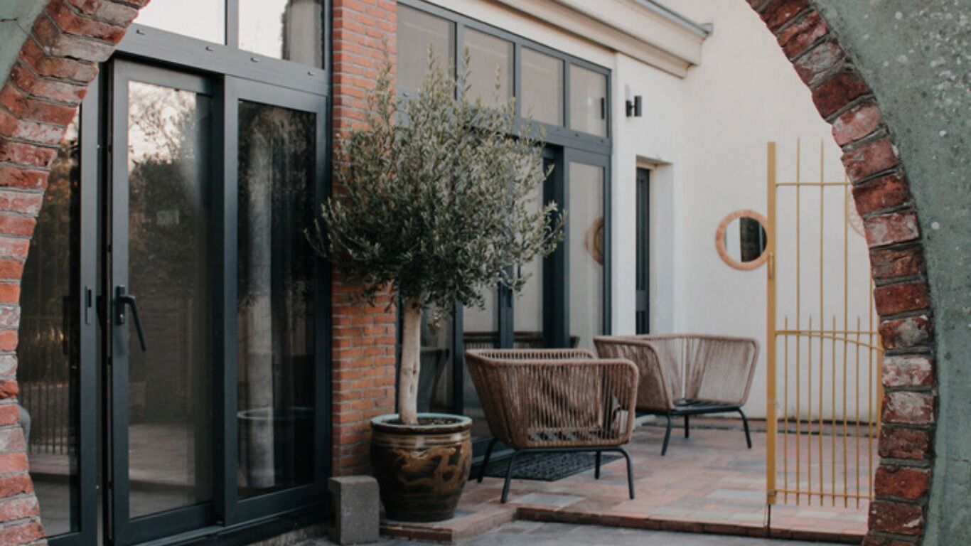 A patio area with a brick wall, a potted plant, wicker furniture, and a metal gate.