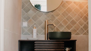 A bathroom with a round mirror, a black sink, and a bottle of hand soap.