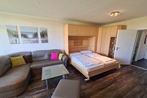 Una habitación compacta con cama, sofá, una mesita y una puerta que da a otra habitación.