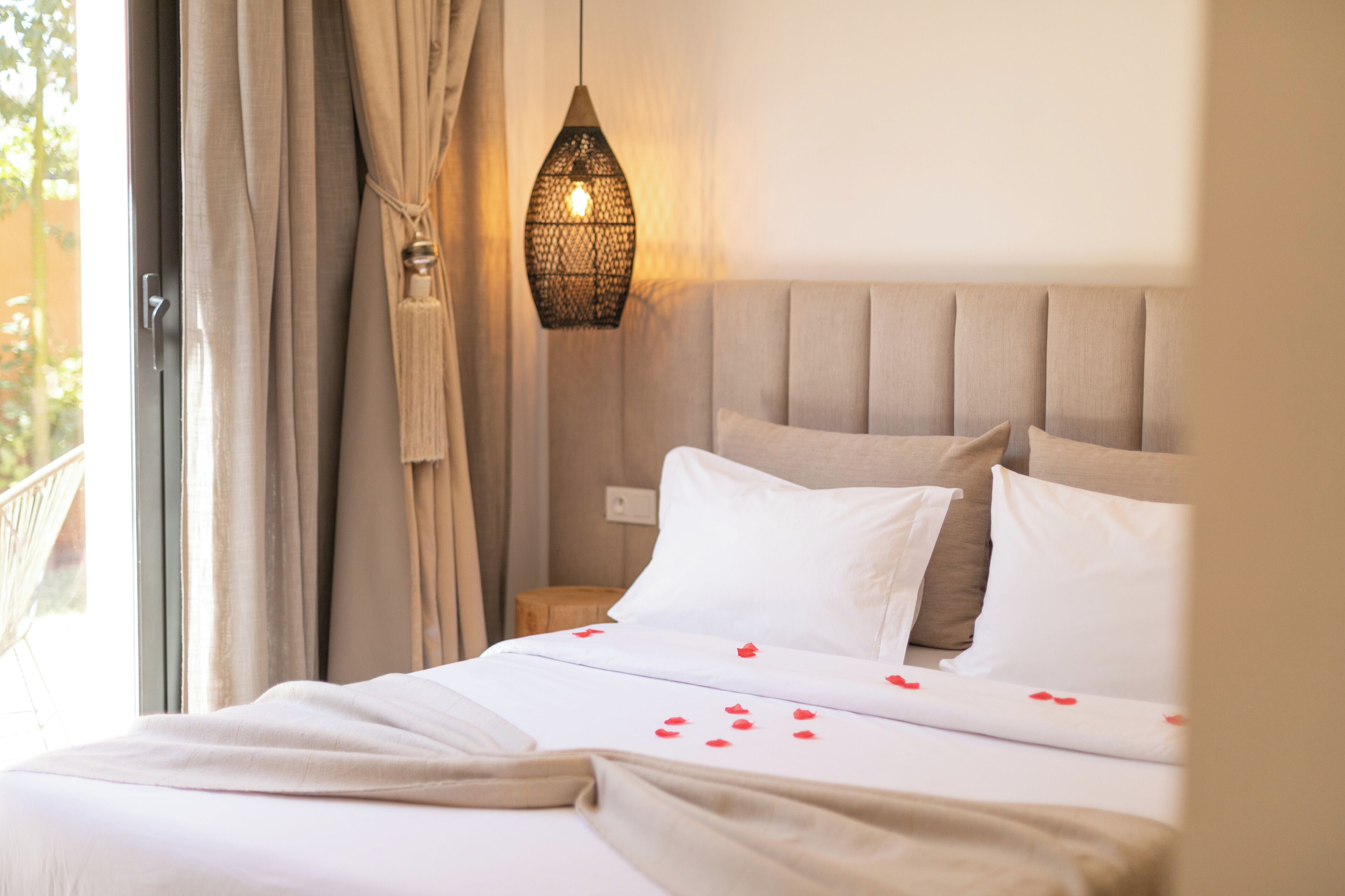 Een hotelkamer met een bed, gordijnen, een hanglamp en uitzicht op het omliggende landschap.