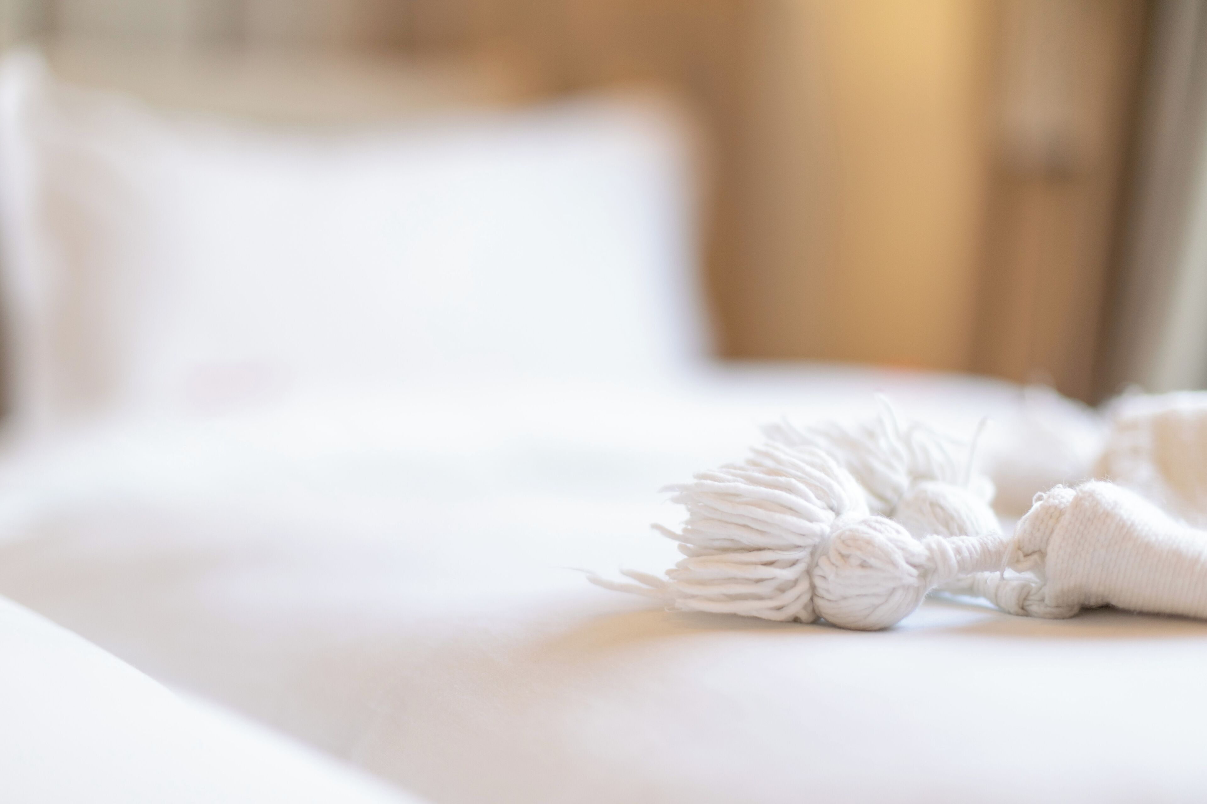 Un lit bien fait, recouvert d’une courtepointe blanche, et agrémenté d’un objet décoratif blanc posé sur le lit.