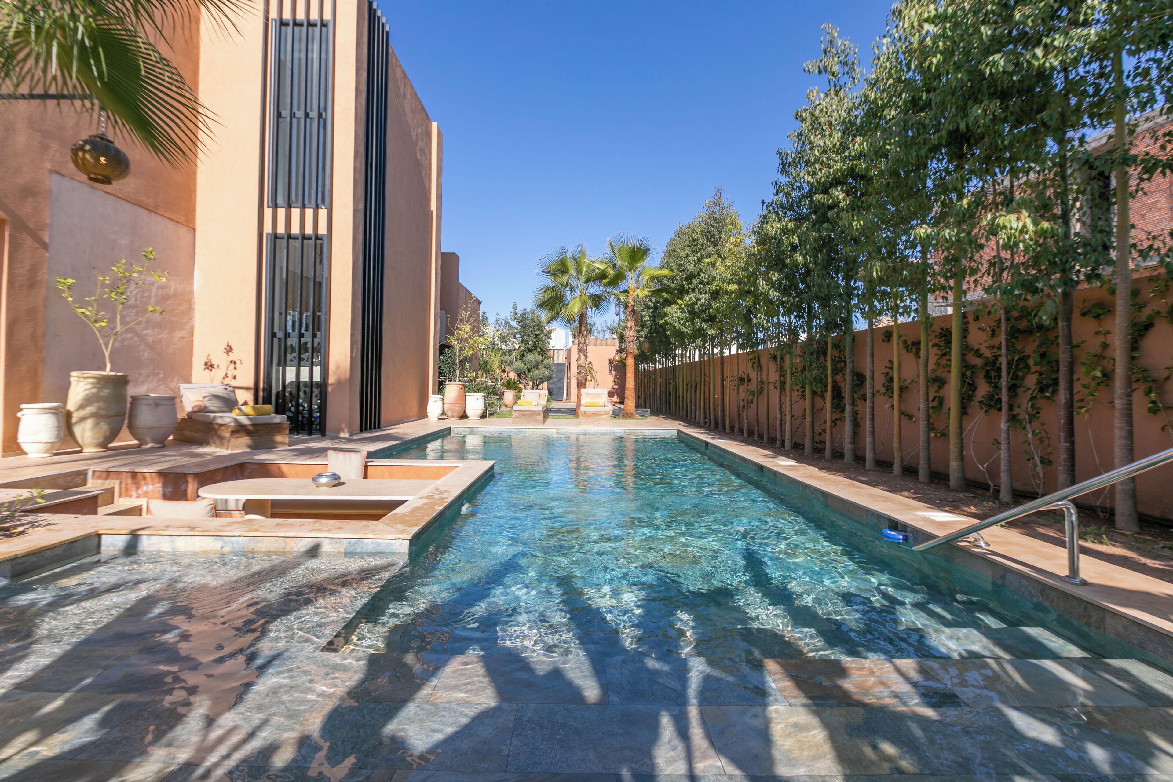 A pool area with clear water, surrounded by trees and a building with a modern design.