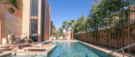 Ein Poolbereich mit klarem Wasser, umgeben von Bäumen und einem Gebäude im modernen Stil.