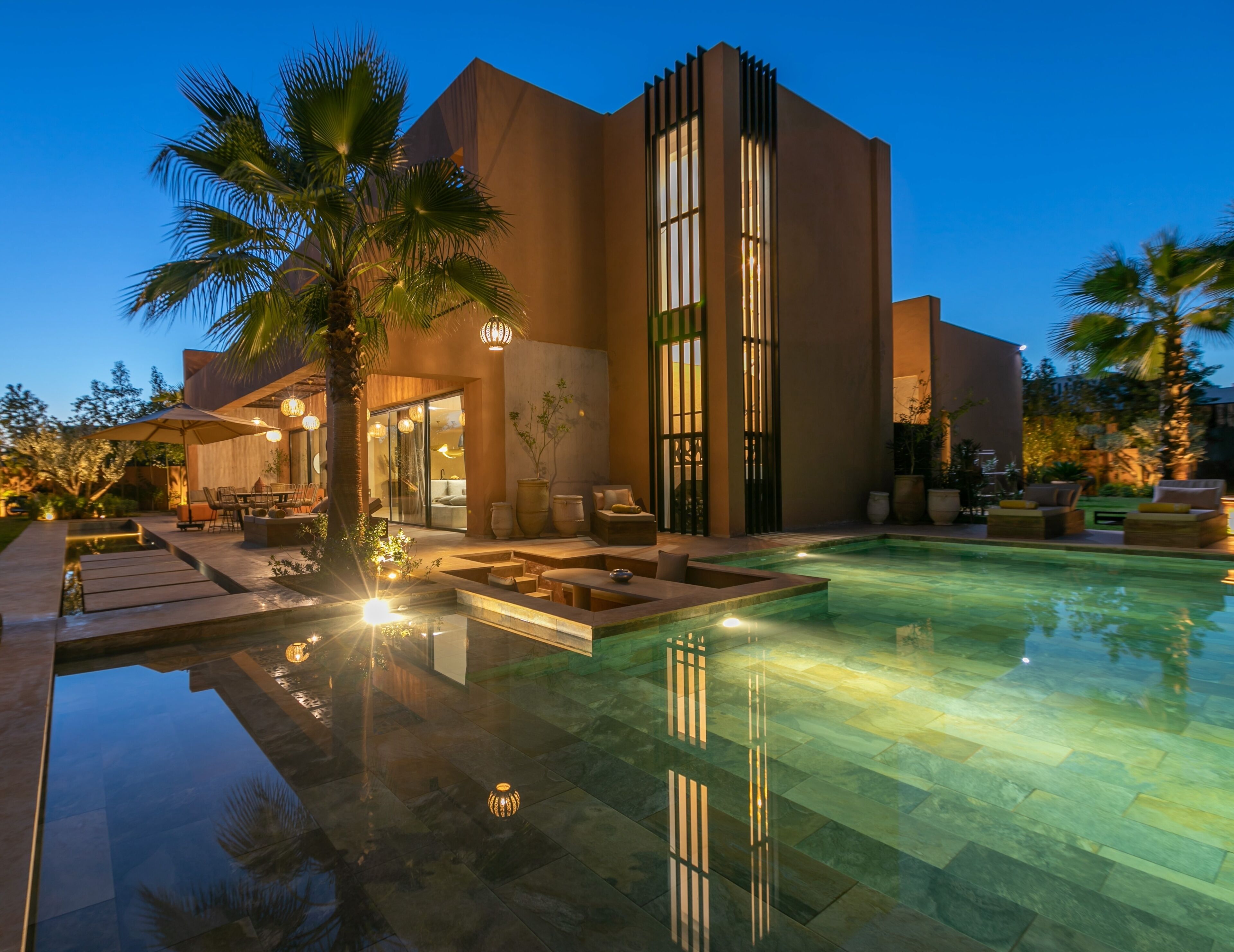 A modern building with a swimming pool, outdoor seating, and palm trees.