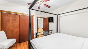 A bedroom with a bed, a wooden wardrobe, a desk with a chair, a ceiling fan, and a television mounted on the wall. - Scott C.H. (Chicago)