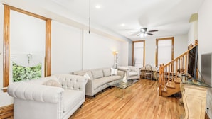 A spacious living room with a large sofa, a glass coffee table, a wooden staircase, and a ceiling fan. - Scott C.H. (Chicago)