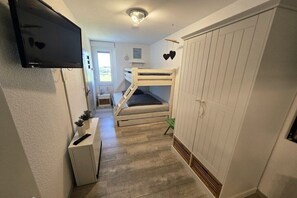 A bedroom with bunk beds, a TV mounted on the wall, a bedside table, and a wardrobe. - South Beach South 002 (Burg-Tiefe)