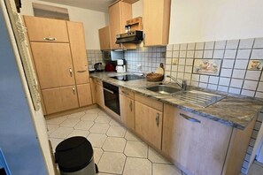 A compact kitchen with wooden cabinets, a built-in oven, a coffee maker, and a sink. - South Beach South 002 (Burg-Tiefe)