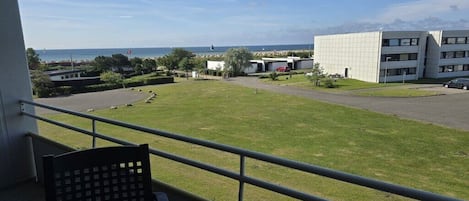 A balcony with a view of a grassy area, a parking lot, and a modern building with multiple windows.