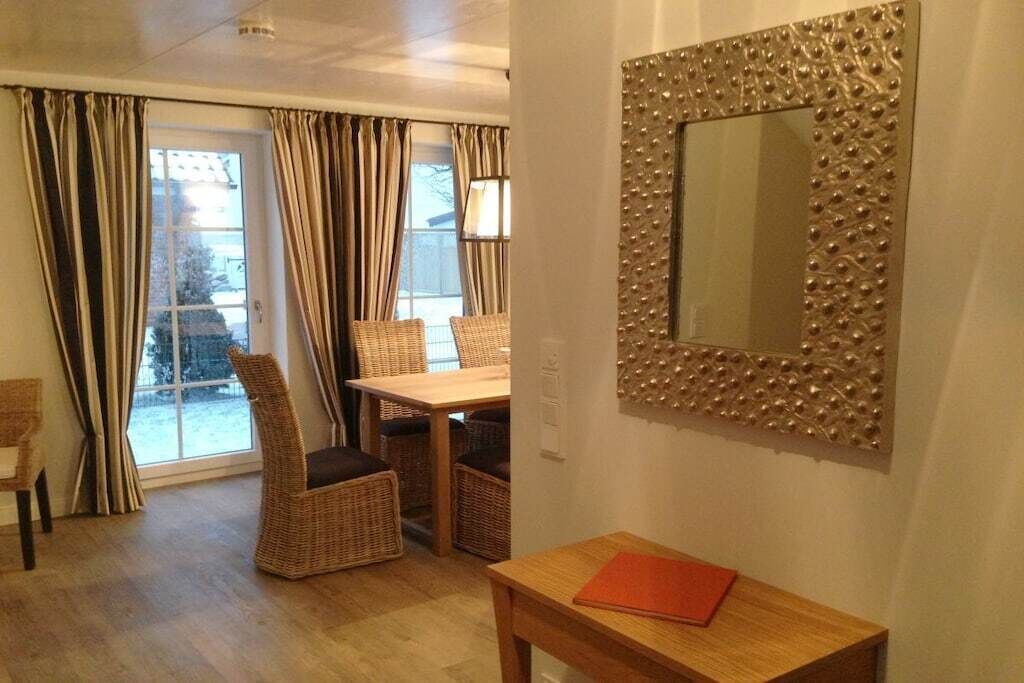 A dining area with wicker chairs and a table, a mirror with a decorative frame, and a window with curtains.
