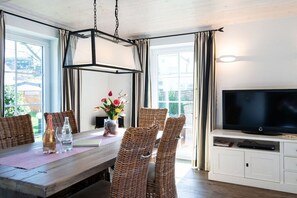 A dining area with wicker chairs, a wooden table, a vase with flowers, and a television on a cabinet. - Holiday home in Sylt with 3 bedrooms (Westerland)