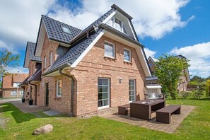 A two-story brick house with a sloped roof, a patio with outdoor furniture, and a well-maintained lawn. - Holiday home in Sylt with 3 bedrooms (Westerland)