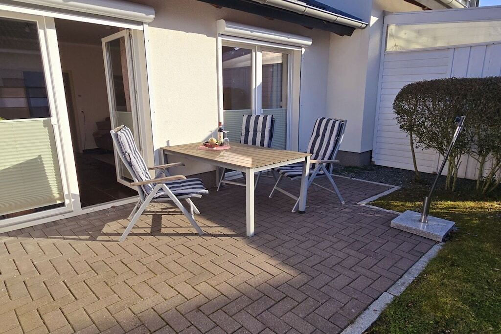 An outdoor patio with a table and chairs, a small garden area, and a white fence.
