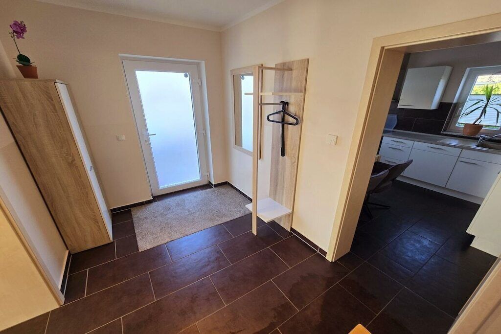 A hallway leading to a kitchen with a door, a coat rack, and a potted plant.