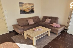 A living room with a brown sofa set, a wooden coffee table, and a painting on the wall. - Pure Holiday Castle 007 (Burg auf Fehmarn)