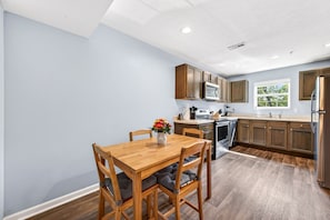 A modern kitchen with wooden cabinets, stainless steel appliances, and a dining area with a wooden table and chairs. - Roadmap Lodging: Central J, 2BR Downtown Apartment, Monthly (Columbus)