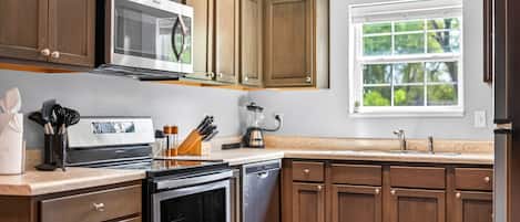 A kitchen with wooden cabinets, stainless steel appliances, a window with a view of greenery, and a countertop with various kitchen items.