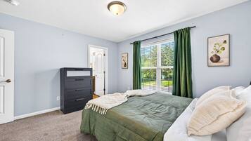 A bedroom with a bed, a dresser, a window with curtains, and a door.
