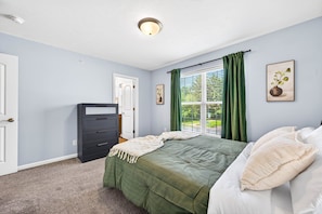 A bedroom with a bed, a dresser, a window with curtains, and a door.