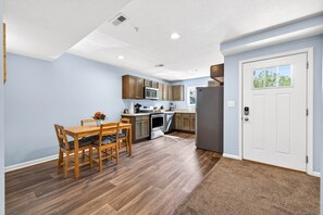 Cocina compacta con armarios de madera, una mesa de comedor con sillas y un refrigerador.