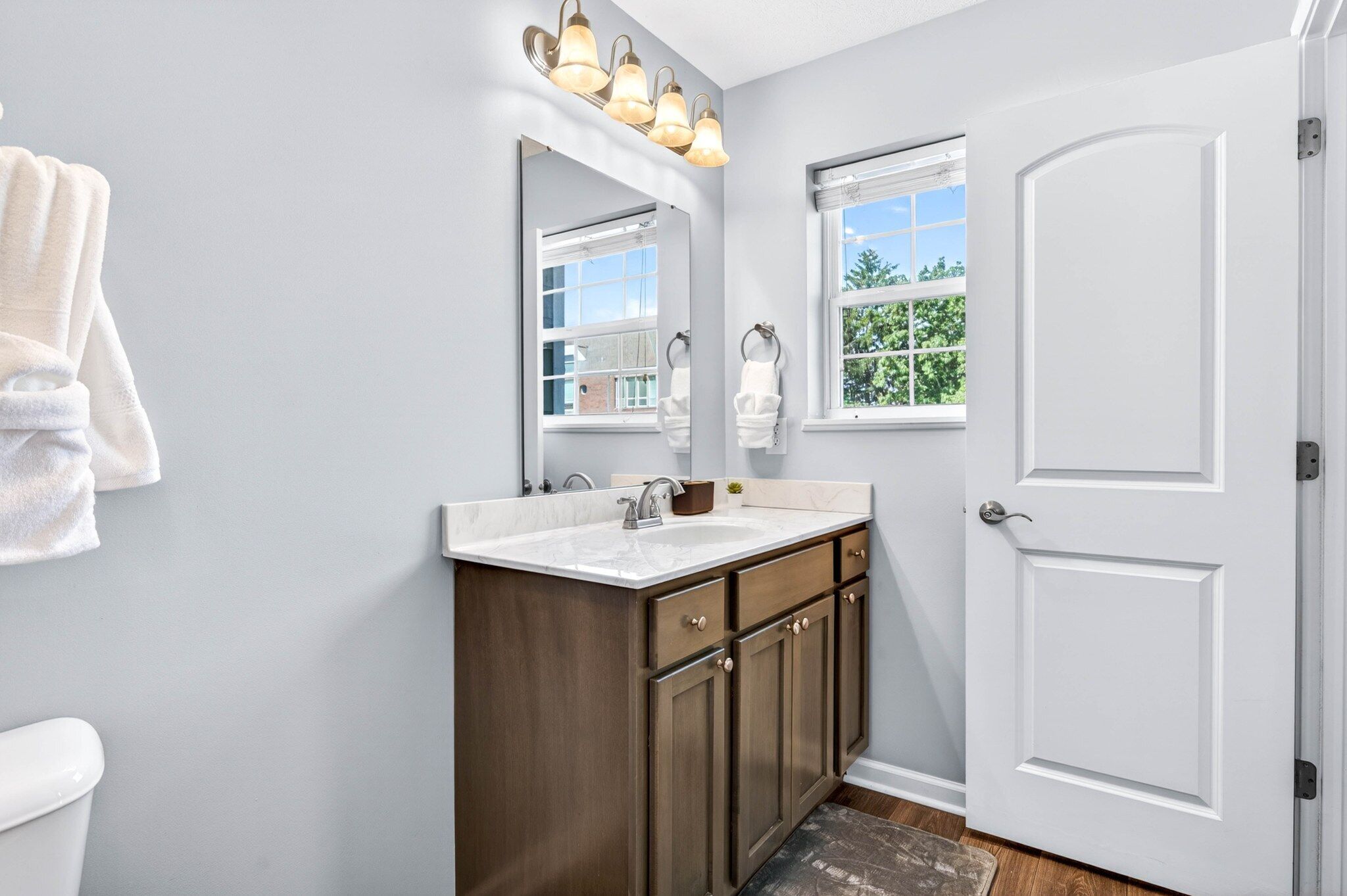 A bathroom with a white door, a sink with a mirror above it, and a window with a view of trees.
