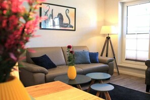 A living room with a sofa, two round tables, a lamp, and a window. - Bernstein Suite & Breakfast Apartment 01 (Büsum)