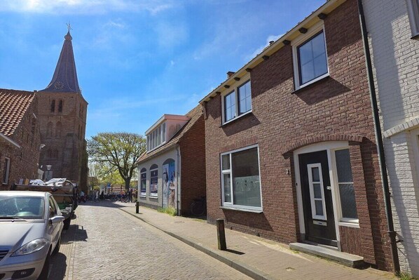 A cobblestone street with traditional brick buildings, a church tower, and a parked car. - Holiday home in Domburg with swimming pool (Domburg)