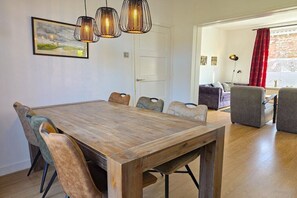 A dining area with a wooden table and chairs, pendant lights, and a door leading to another room. - Holiday home in Domburg with swimming pool (Domburg)