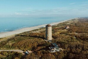 A coastal landscape with a water tower, beach, and a building surrounded by trees. - Holiday home in Domburg with swimming pool (Domburg)