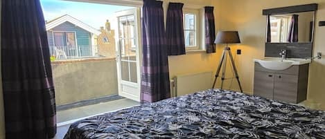 Un dormitorio con cama, ventana, espejo y baño con lavamanos.